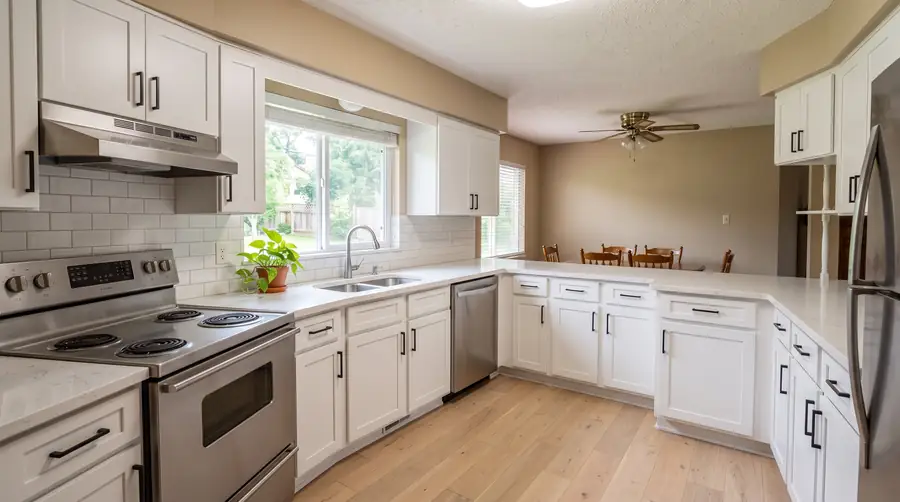 The same kitchen after: white shaker cabinets, light stone counters, a subway-tile backsplash, stainless appliances and a light wood floor.