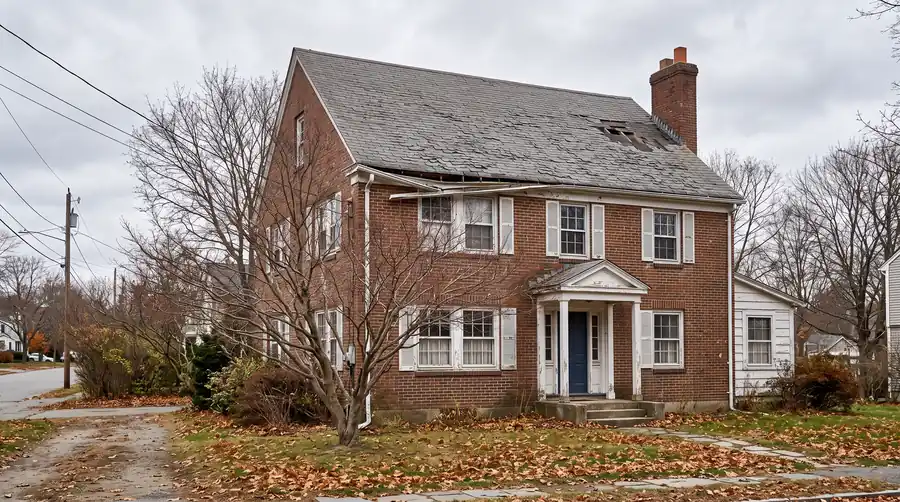 The house before: a brick colonial with faded, curling shingles, a sagging gutter and missing shingles by the chimney.